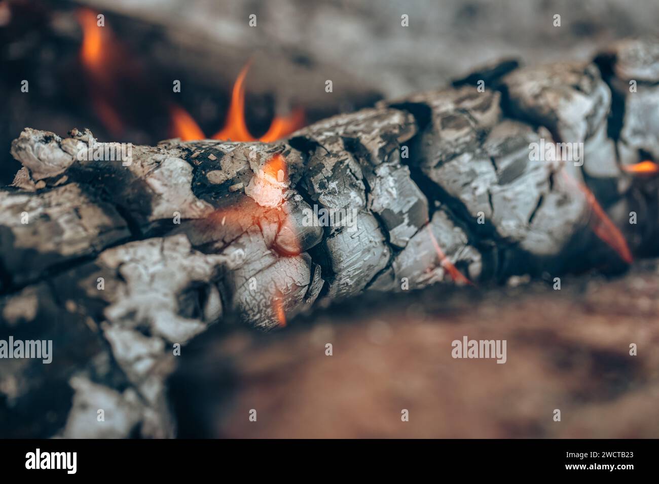 Nahaufnahme von glühender Glut mit kleinen Flammen, gekennzeichnet durch Orangentöne, in den Resten eines Holzfeuers Stockfoto