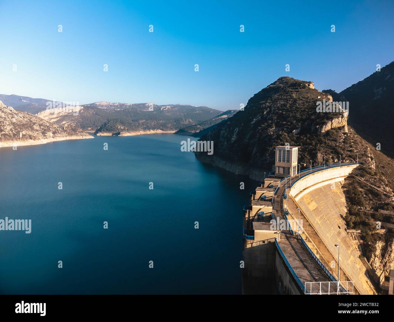 Klarer Himmel über einem großen Damm, der tiefblaues Wasser in einer zerklüfteten Bergkulisse zurückhält Stockfoto