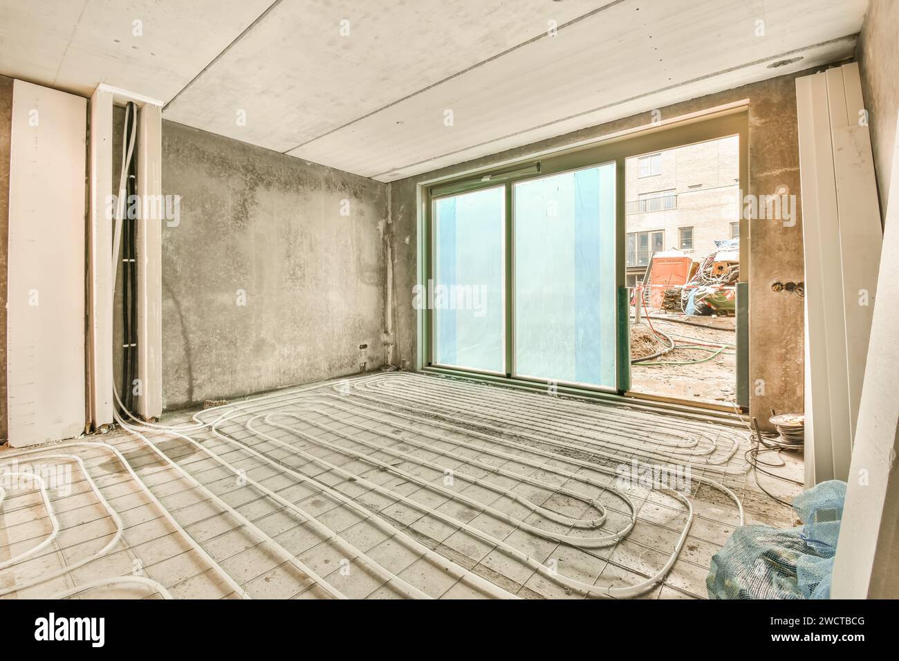 Eine Fußbodenheizung, die auf einem Betonboden in einem im Bau befindlichen Raum angeordnet ist, mit großen Fenstern und unfertigen Wänden. Stockfoto
