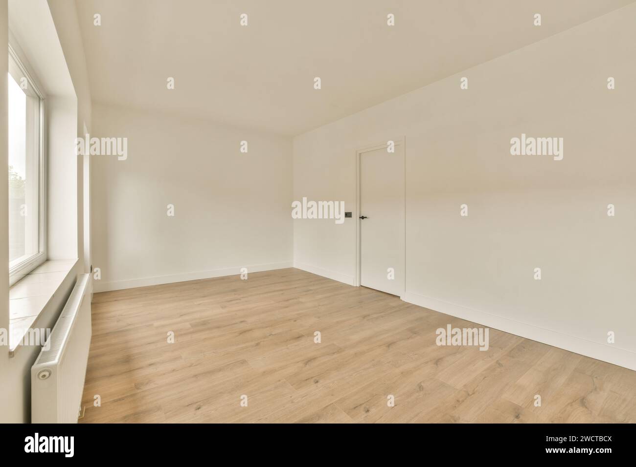 Ein geräumiger, leerer Raum mit großem Fenster, cremefarbenen Wänden und Laminatfußboden, beleuchtet durch Tageslicht. Stockfoto