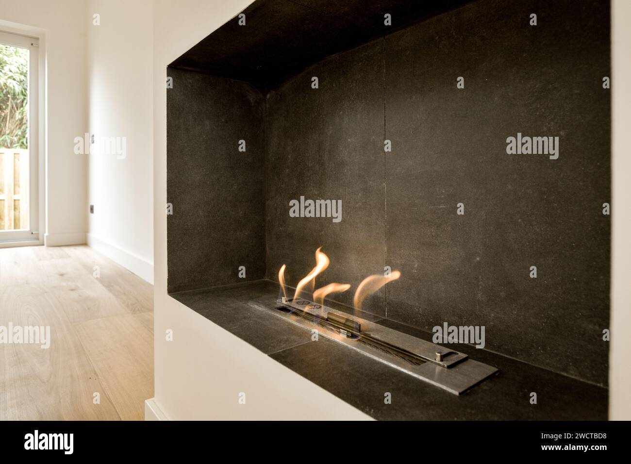 Ein moderner Bioethanol-Kamin mit eleganter, dunkler Einfassung, der ein warmes Ambiente in minimalistischer Inneneinrichtung bietet. Stockfoto
