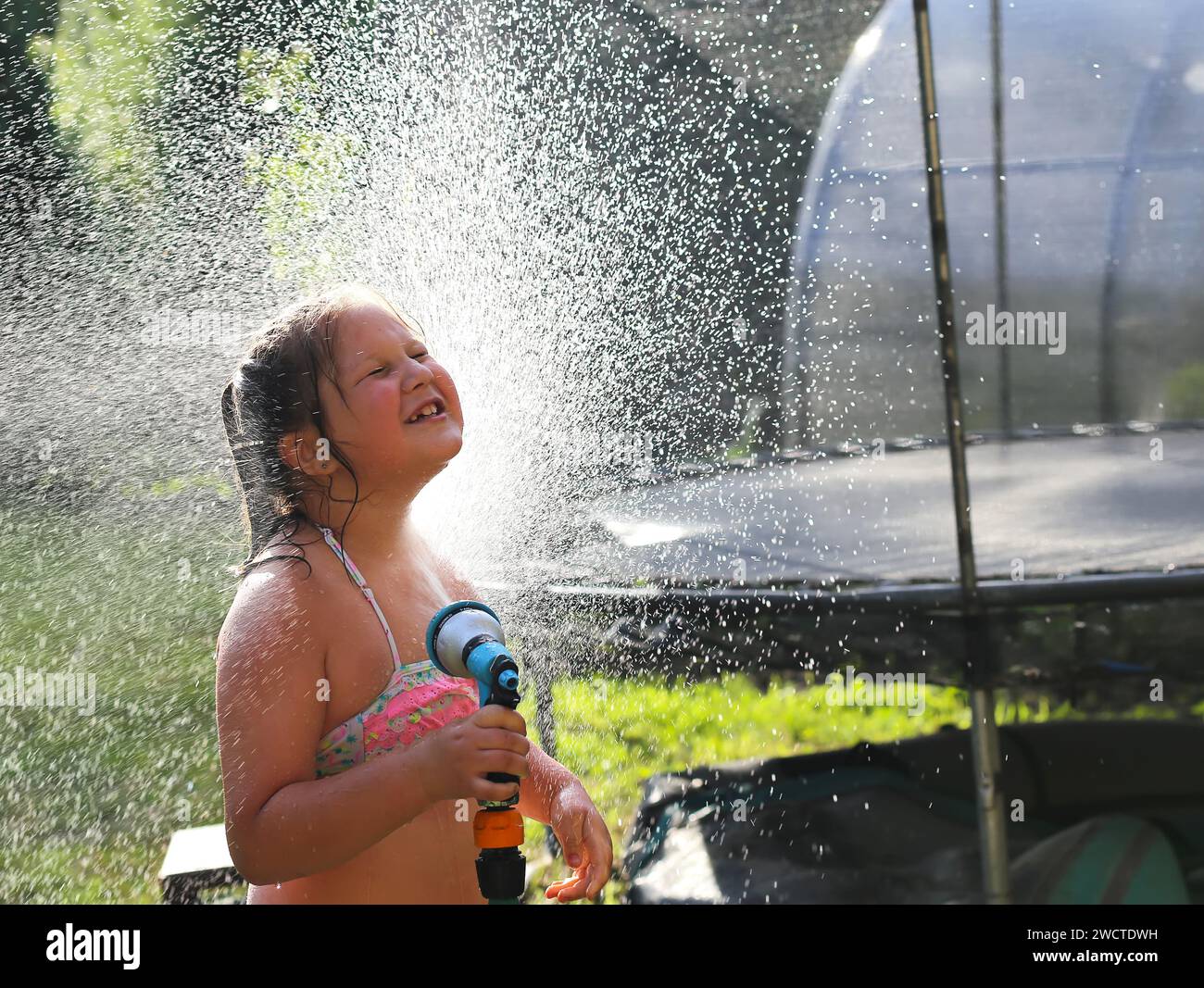 Kleine Mädchen spritzen mit Wasser, um sich in den Sommerferien abzukühlen. Fröhliches, glückliches Kind Stockfoto