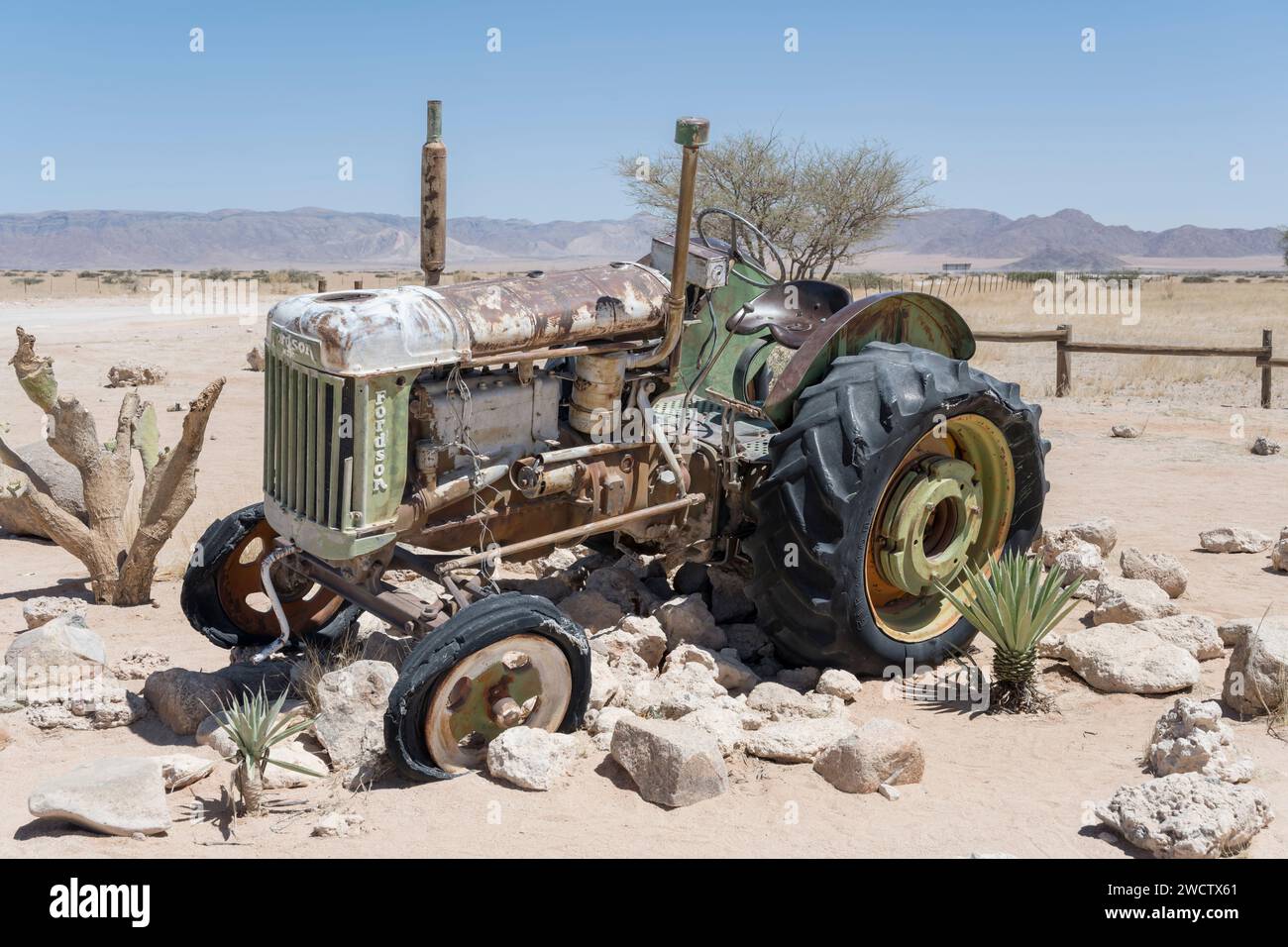 Vintage-Traktorwrack, das durch Rost in der Ausstellung an der Tankstelle in der Wüste Naukluft abgenutzt wurde, im hellen Licht des späten Frühlings in Solitaire, Namibia, AFR Stockfoto