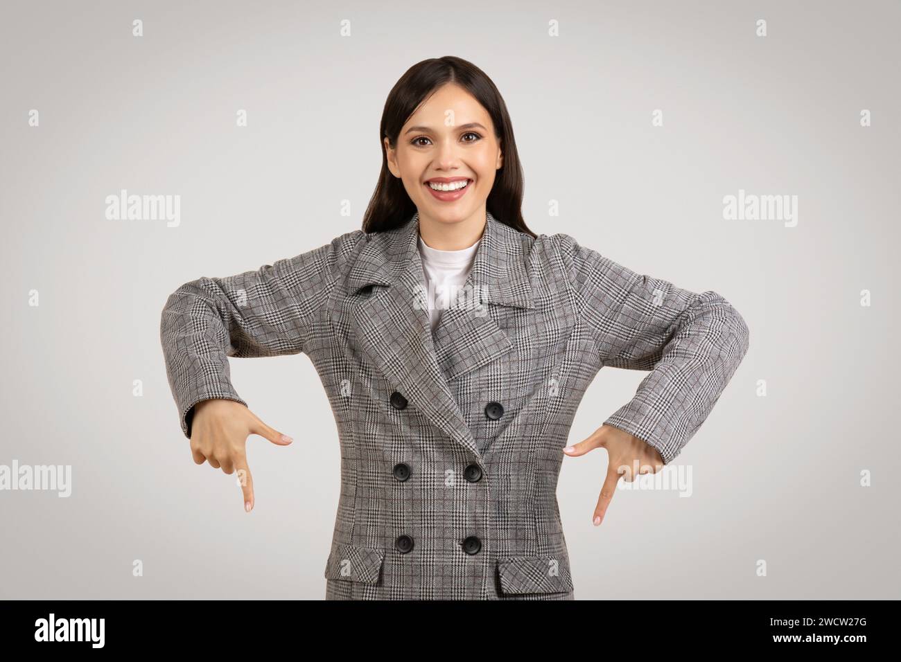 Glückliche Frau in einer Jacke, die mit beiden Händen nach unten zeigt Stockfoto