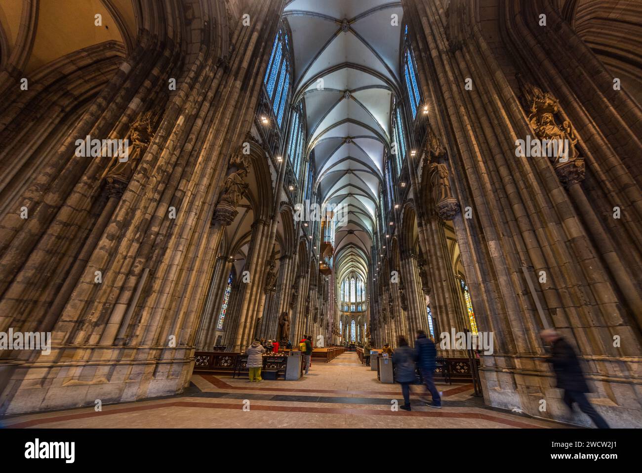 Besucher durchqueren das Langhaus im Kölner Dom in Köln, Nordrhein-Westfalen, Deutschland. Schlanke Bündelpfeiler stützen das 43,35 Meter hohe Rippengewölbe, eines der höchsten aller gotischen Kathedralen. Der Bau der Kathedrale begann 1248 und wurde nach einer jahrhundertelangen Unterbrechung erst 1880 fertiggestellt. Mit 157 Metern sind ihre beiden Türme die höchsten aller zweitürmigen Kirchenfassaden der Welt; die Kathedrale ist seit 1996 UNESCO-Weltkulturerbe. Stockfoto