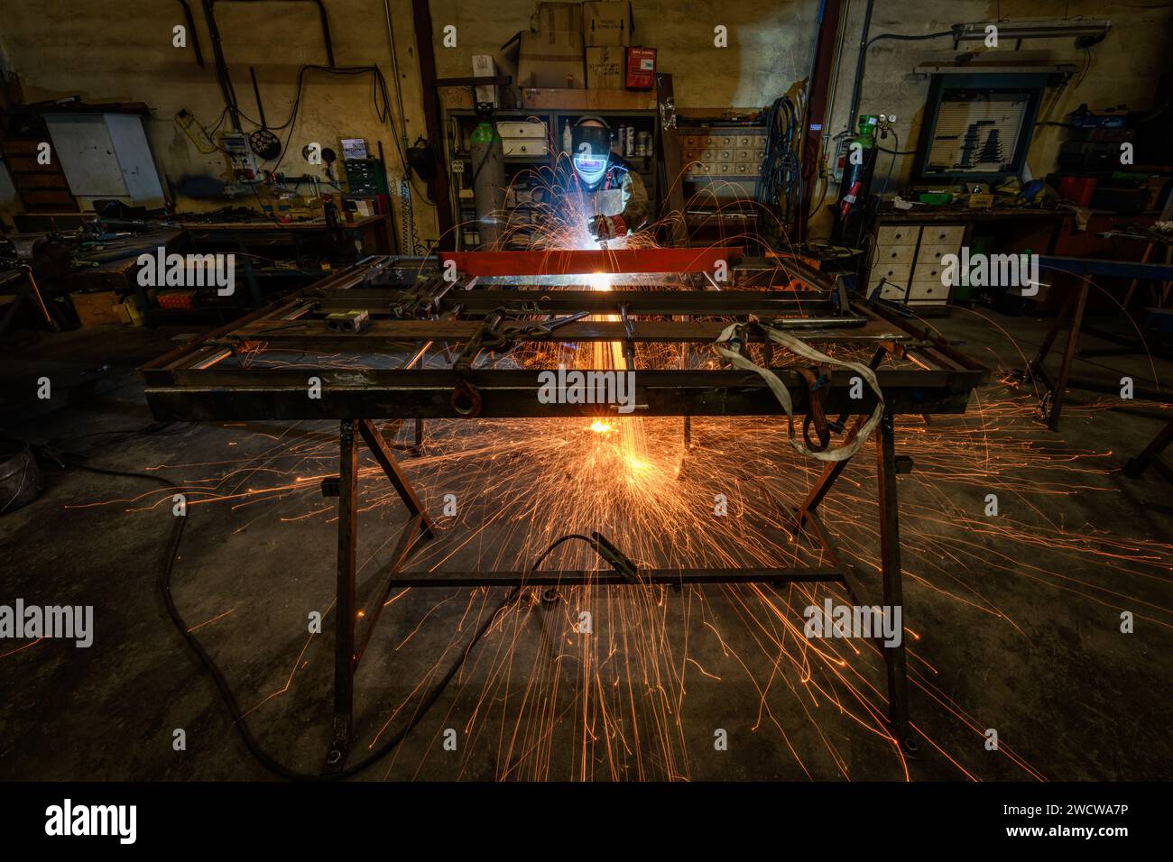 Ein Schweißer, der in einem Metallverarbeitungsunternehmen arbeitet, schweißt Eisenstangen mit vielen Funken Stockfoto
