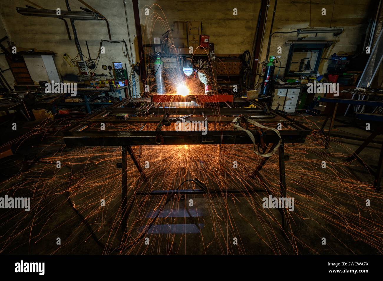 Ein Schweißer, der in einem Metallverarbeitungsunternehmen arbeitet, schweißt Eisenstangen mit vielen Funken Stockfoto