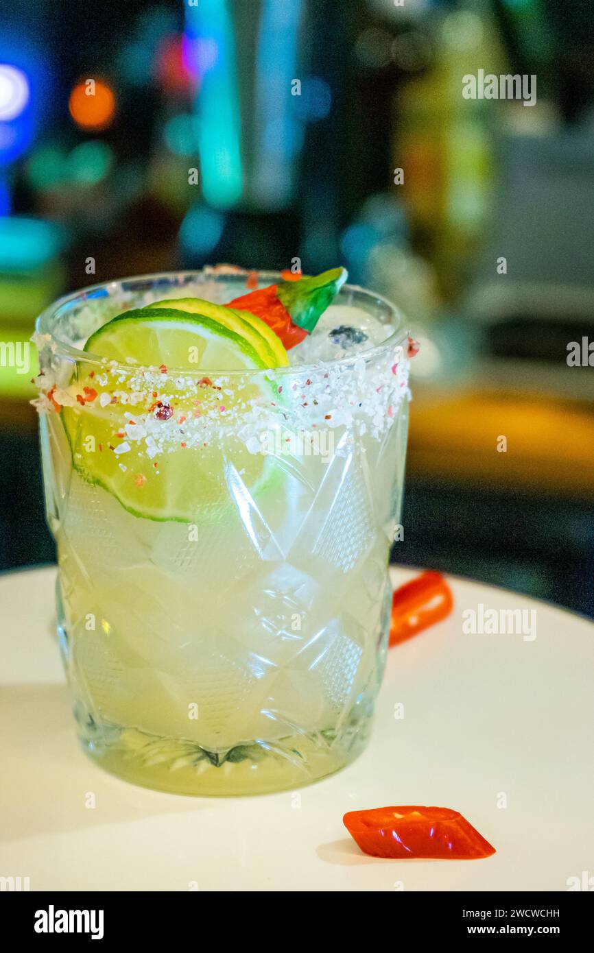 Ein erfrischender Margarita-Cocktail, garniert mit einer Limettenscheibe und einem Hauch Chili-Pulver, wird elegant auf einem weißen Teller präsentiert. Stockfoto