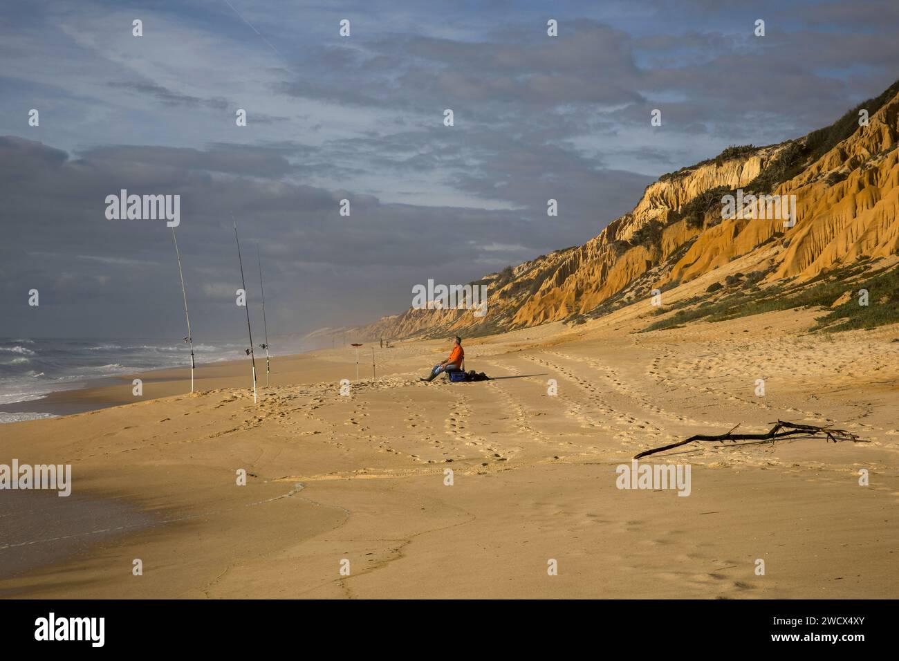 Portugal, Alentejo, Gale Fontainhas Beach, Fischer sitzen am Strand, wo seine Angelruten zwischen dem Atlantischen Ozean und ockerfarbenen fossilen Klippen gepflanzt werden, die fünf Millionen Jahre alt sind Stockfoto