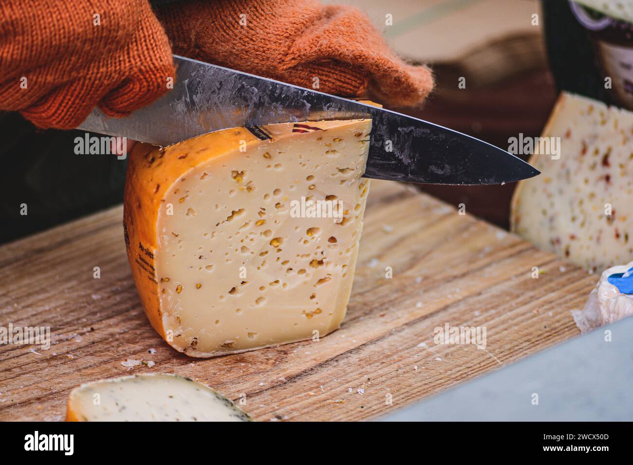 Hände einer Frau, die mit einem Messer ein Stück selbstgemachten Bio-natürlichen lettischen Käse auf einem Straßenmarkt schneidet Stockfoto