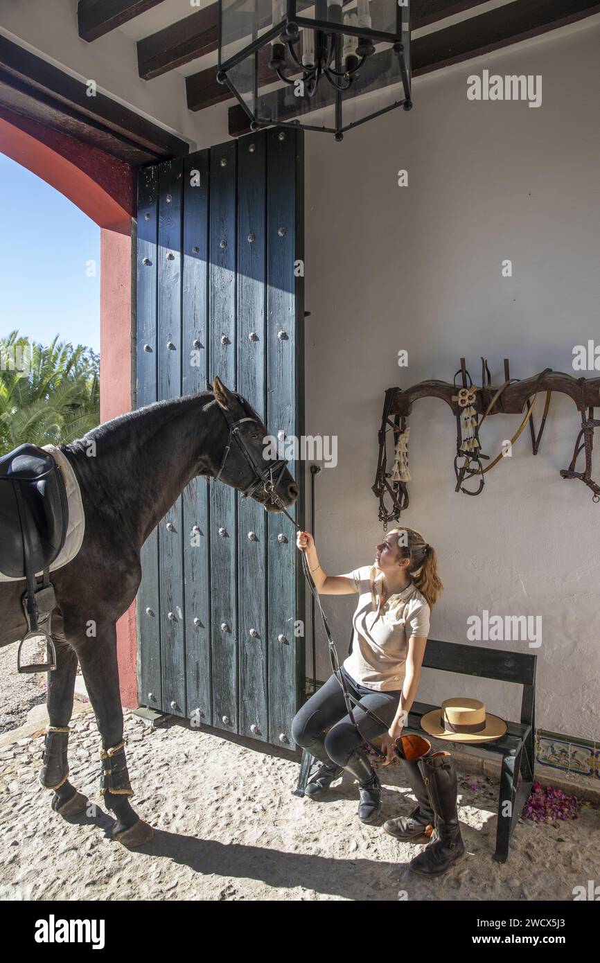 Spanien, Andalusien, Moron de la Frontera, Hacienda las Alcabalas, junger Reiter mit schwarzem Pferd und Reitausrüstung im Vorraum einer andalusischen Hacienda Stockfoto