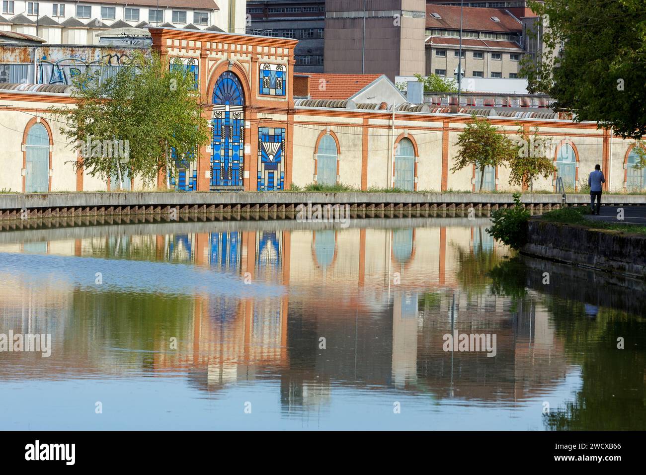 Frankreich, Meurthe et Moselle, Nancy, Flussufer des Nancy-Kanals zwischen Marne und Rhein, Fassade des ehemaligen Industriewerks Alsthom, Streetart an der Fassade von Straßenkünstlerin Koralie, die im Rahmen ihres Projektes Nomade entstanden ist und Buntglasfenster im Art déco-Stil aus Textil darstellt Stockfoto