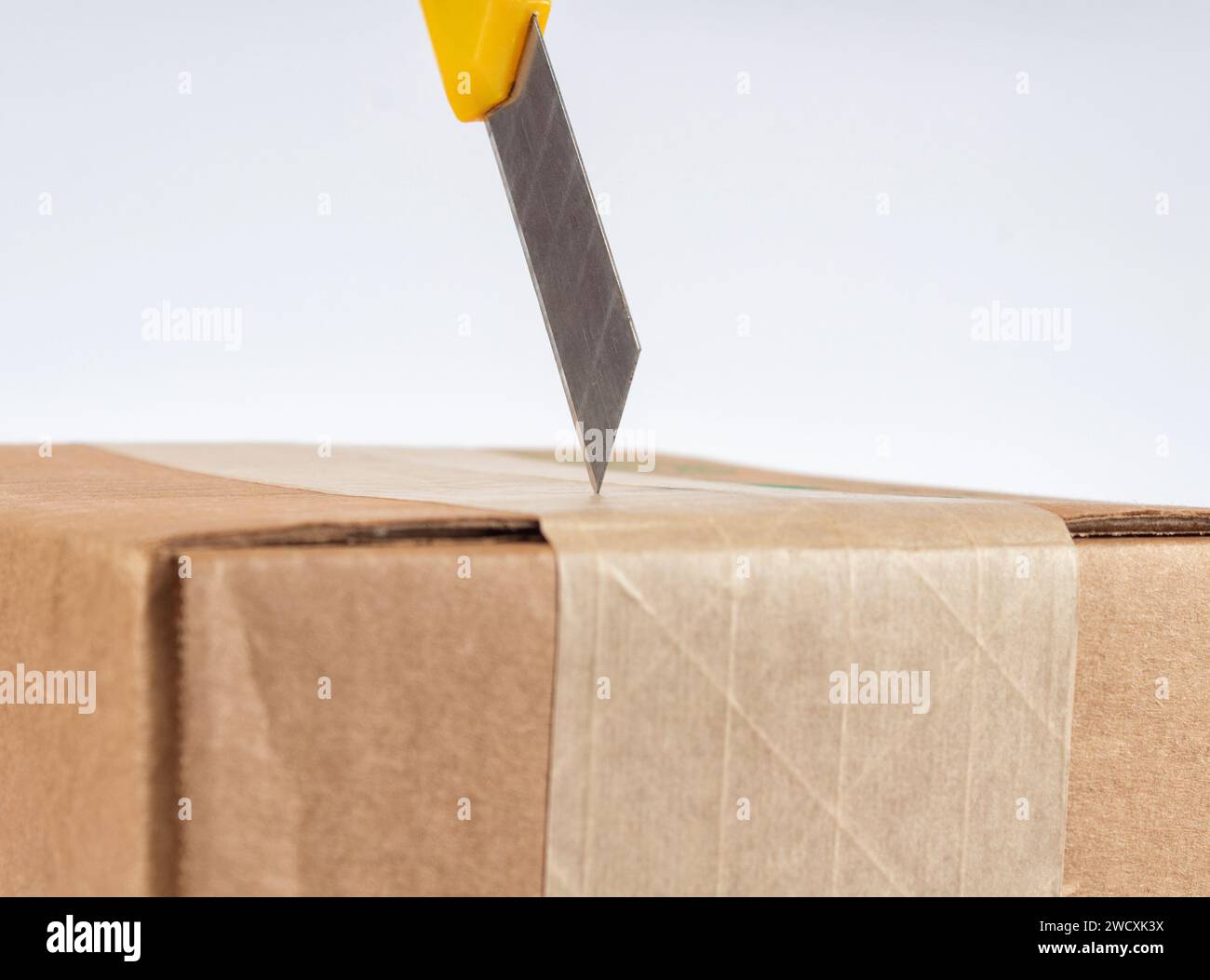 Öffnen des Kartons mit gelbem Schreibwarenmesser. Nahaufnahme. Stockfoto