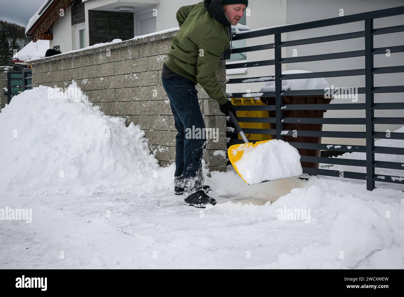 Ein Mann in Jacke, Hut und Handschuhen schaufelt Schnee vor dem Haus nach dem Schneesturm - Nahansicht. Stockfoto