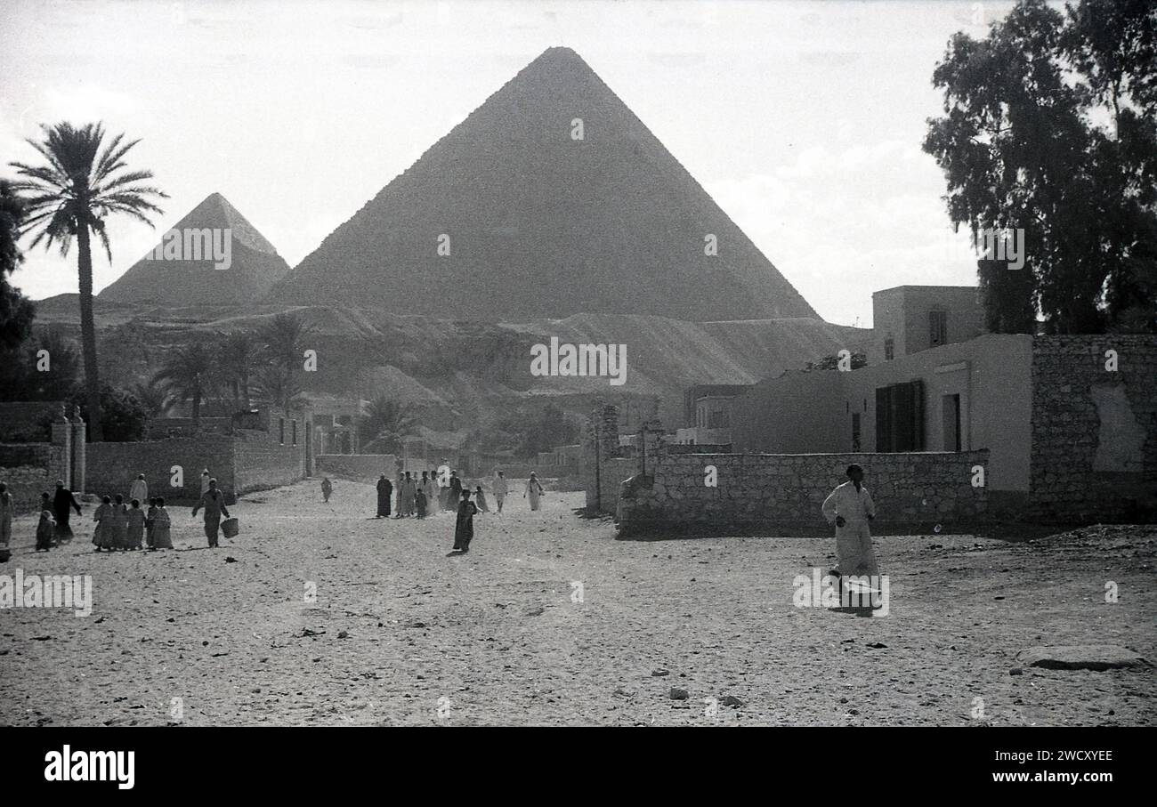 1950er Jahre, historisch, Ägypten, Einheimische spazieren durch eine staubige Gegend in Gizeh, mit einer Pyramide im Hintergrund, ein klassisches Symbol dieses alten Landes an der nordöstlichen afrikanischen Küste, die Afrika mit dem Nahen Osten verbindet. Zu den historischen Denkmälern zählen die berühmten Pyramiden von Gizeh entlang des fruchtbaren Niltals. Stockfoto