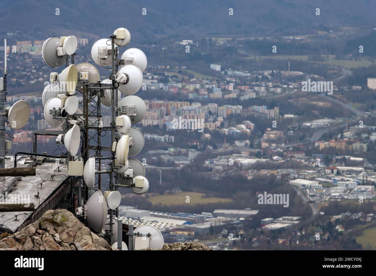 Telekommunikationsgeräte, die an einem Mast auf einem Felsen über der Stadt befestigt sind Stockfoto