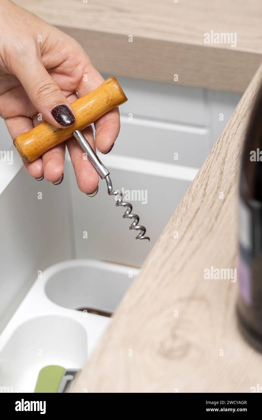 Die Frau hält einen Korkenzieher in der Hand, um eine Flasche Wein zu öffnen. Die Hand einer Frau nimmt einen Korkenzieher aus einer Küchenschublade. Weiblicher Alkoholismus. Vertikales Foto Stockfoto