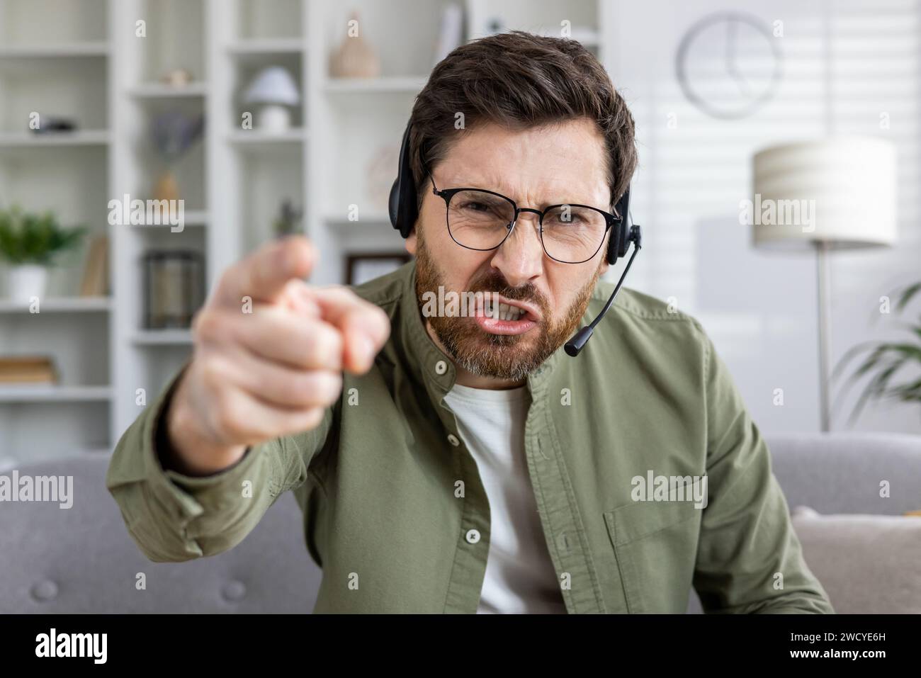 Ein genervter männlicher Telearbeit-Telearbeit in einem Headset, der auf die Kamera zeigt und Stress und Frustration zeigt. Stockfoto