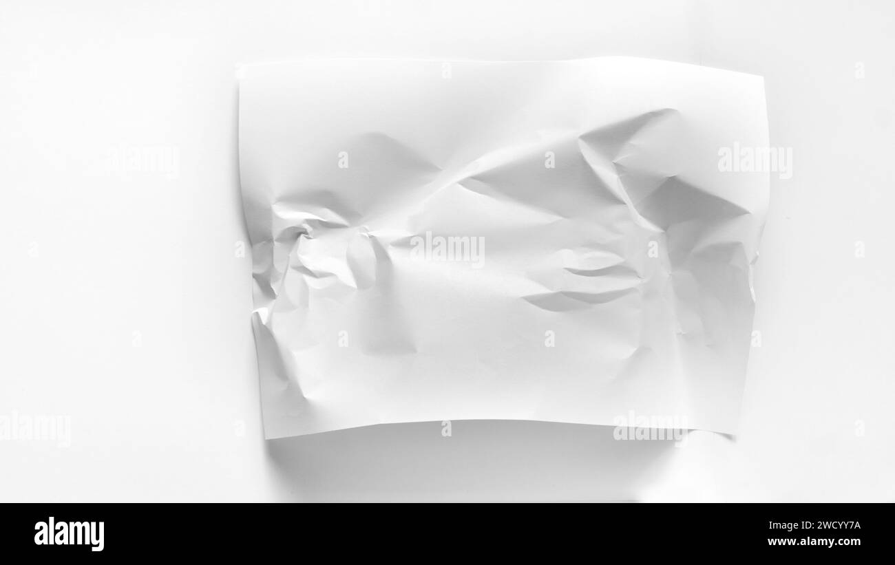 Weißes zerknittertes Blatt Papier in Nahaufnahme mit Kopierraum. Ein weißes leicht zerknittertes A4-Blatt liegt auf weißem Hintergrund. Mockup für Beschriftungen, Wörter, Stockfoto