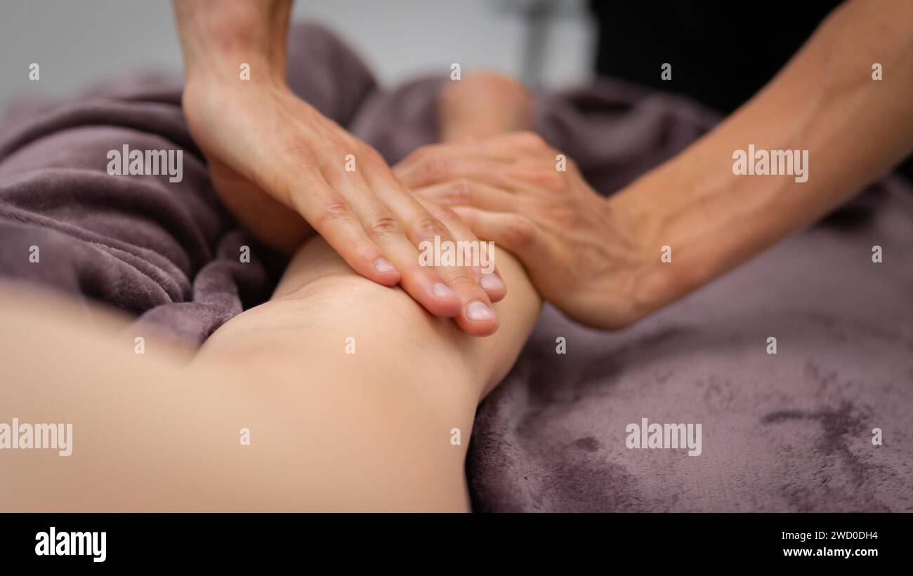 Die erfahrenen Hände eines Masseurs sorgen für eine tiefe Gewebemassage am Bein des Kunden und helfen Ihnen, die Muskelspannung in einer ruhigen Spa-Umgebung zu lindern. Stockfoto