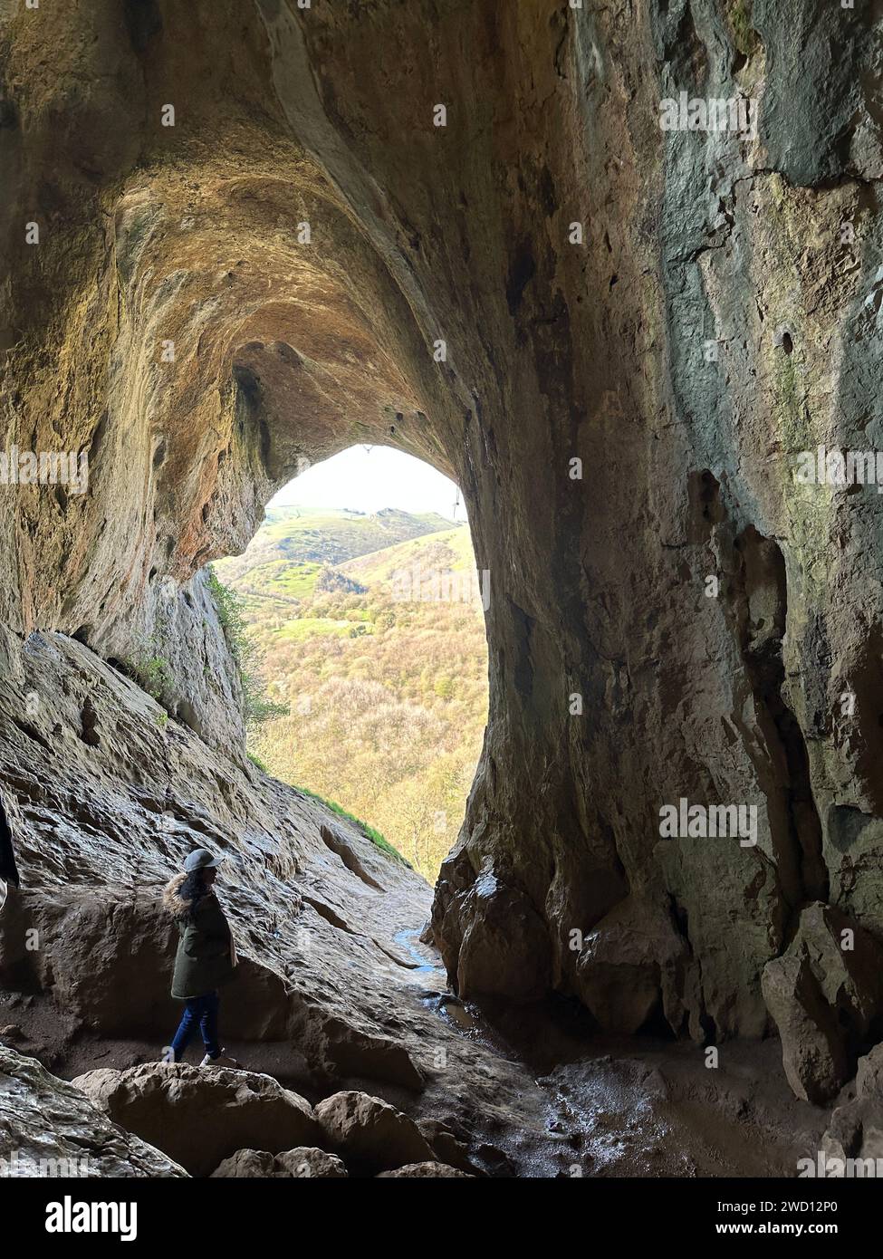 Zwei Individuen erkunden eine schwach beleuchtete unterirdische Höhle, deren Silhouetten von dem schwachen Schein des natürlichen Lichts beleuchtet werden, das durch eine ferne Öffnung gefiltert wird Stockfoto
