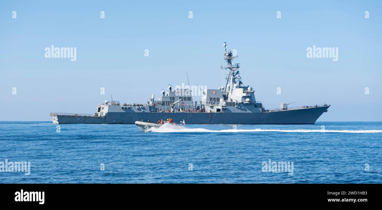 Matrosen manövrieren ein aufblasbares Starrrumpf-Boot in der Nähe des Raketenzerstörers USS Sterett. Stockfoto