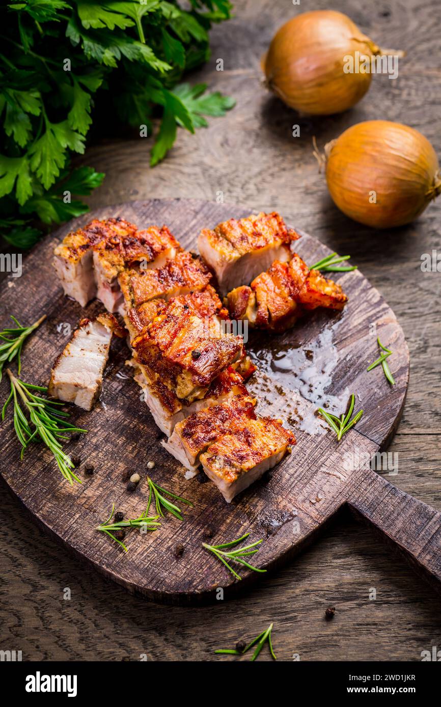 Gegrillter Schweinebauch mit knuspriger Haut, Zwiebeln und Kräutern auf hölzernem Hintergrund Stockfoto