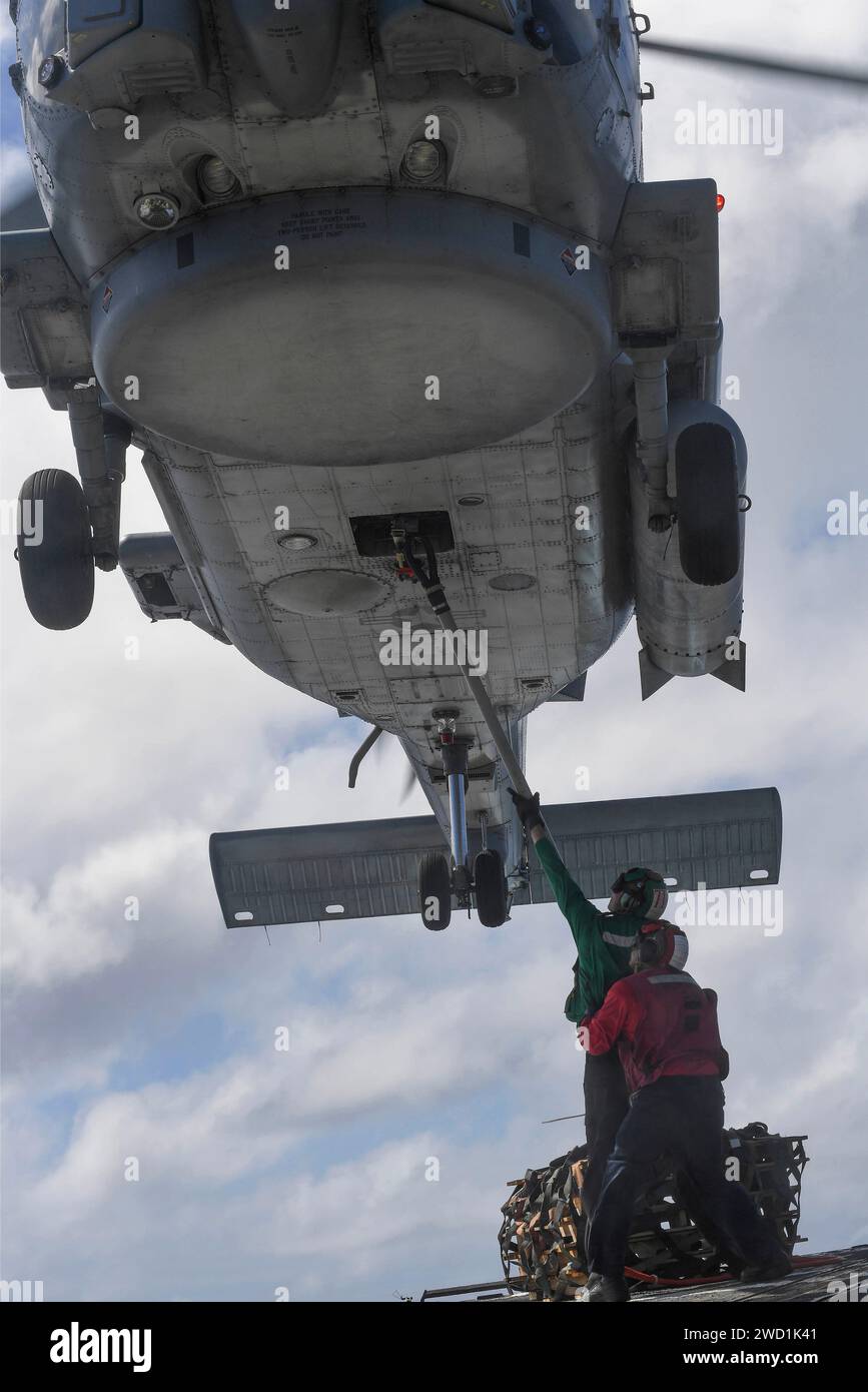 Flieger befestigen den Haken an einem MH-60R Sea Hawk Hubschrauber für eine vertikale Auffüllung auf See. Stockfoto
