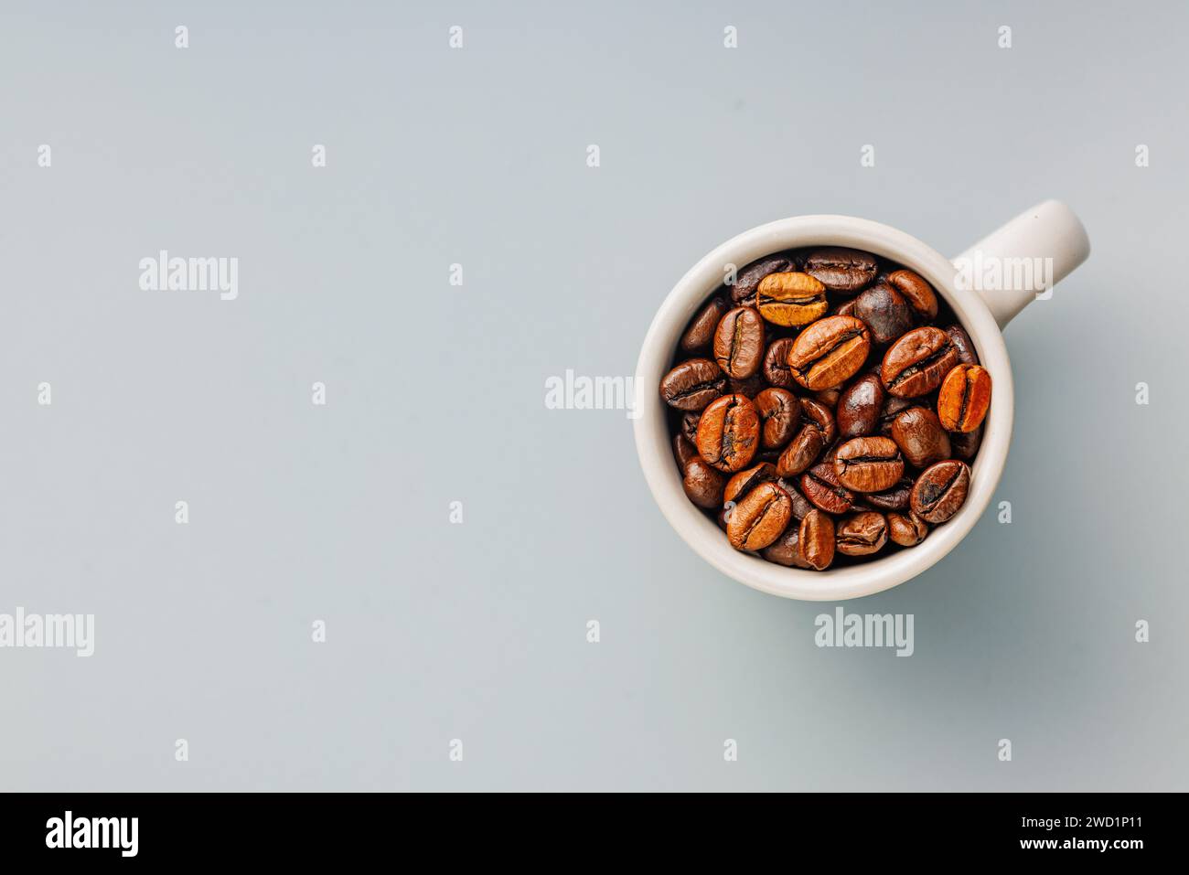 Geröstete Kaffeebohnen in Kaffeetasse auf grauem Hintergrund. Draufsicht. Stockfoto