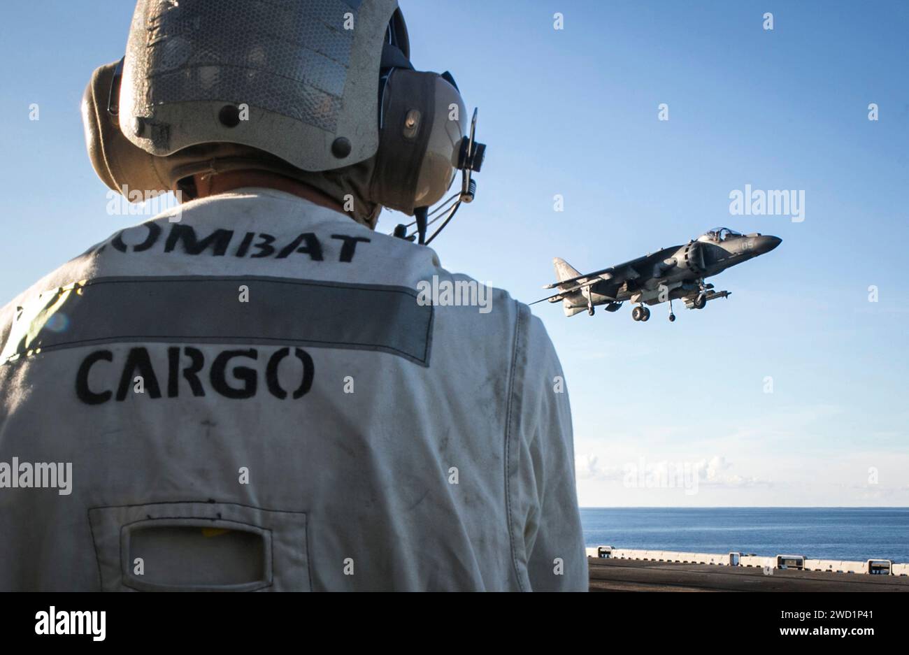 Ein Marine sieht zu, als ein AV-8B Harrier-Flugzeug auf der USS Bonhomme Richard landet. Stockfoto