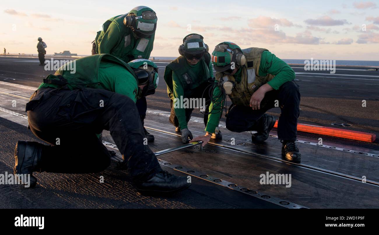 Die Matrosen ziehen die Schrauben auf einer Katapultbahn fest, bevor sie ein Flugzeug an Bord der USS Ronald Reagan starten. Stockfoto