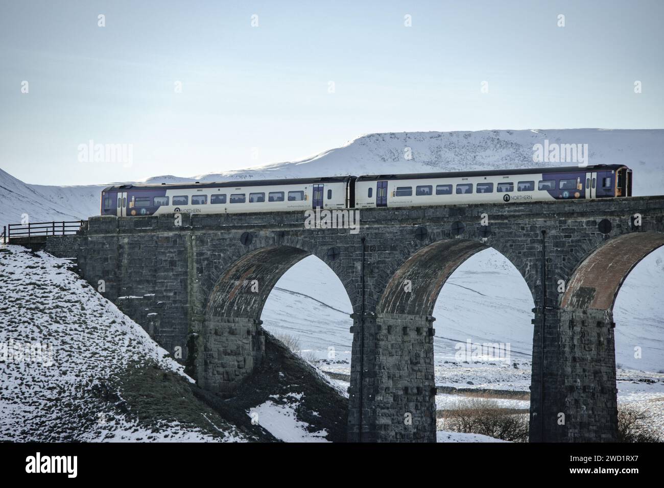 Ein Zug aus dem Norden überquert die Bahn auf dem Ribblehead Viaduct im Schnee im Yorkshire Dales National Park. An einem schönen Tag im blauen Himmel. Stockfoto