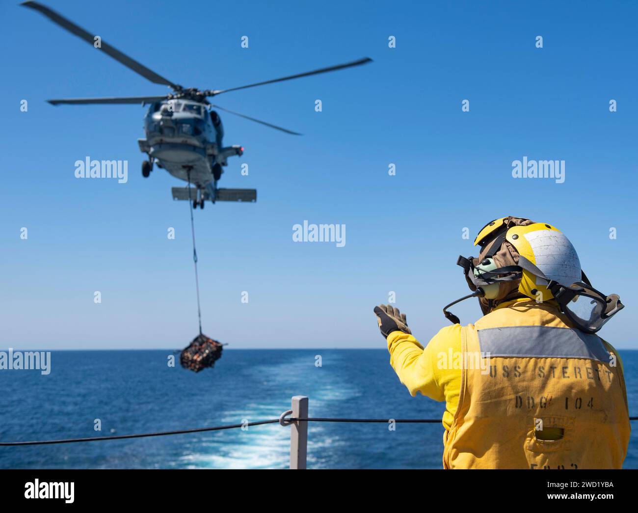 Atswain's Mate signalisiert einem MH-60R Sea Hawk Hubschrauber, Frachtpaletten zu positionieren und abzusenken. Stockfoto