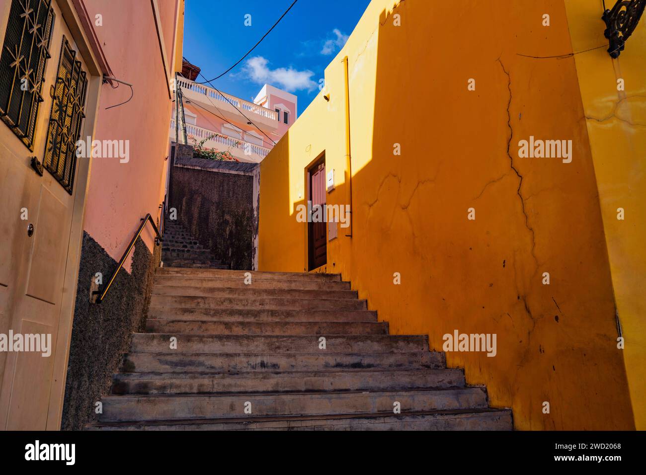Eine lebhafte Treppenaufgangsszene mit warmen gelben Wänden, die den Aufstieg umrahmen und den charmanten Charakter der Straßenarchitektur von Ribeira Grande unter ihnen einfangen Stockfoto