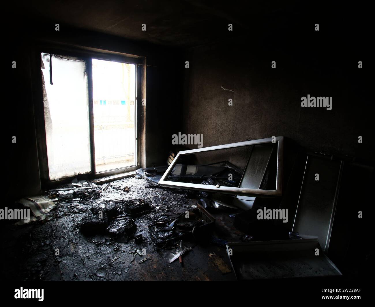 Verbranntes und zerstörtes Zimmer mit hellem Tageslicht von der Balkontür. Stockfoto