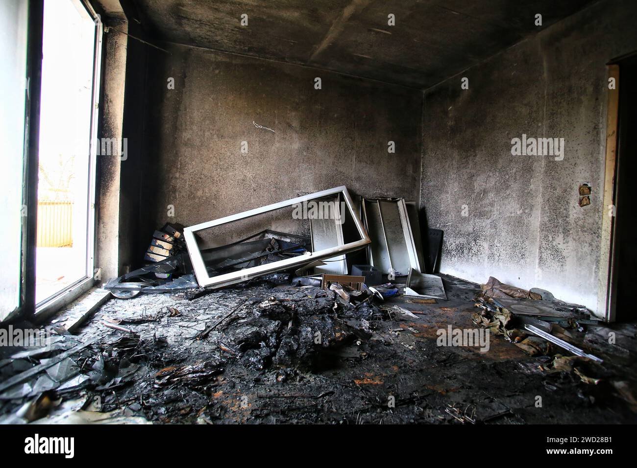 Verbranntes und zerstörtes Zimmer mit hellem Tageslicht von der Balkontür. Stockfoto