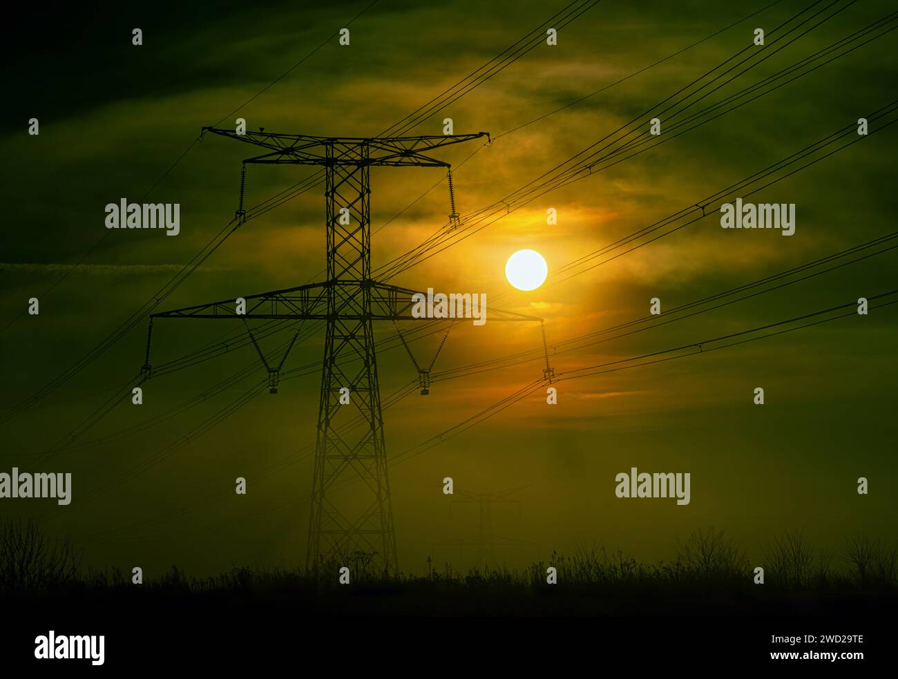 Hochspannungspylon in der Mitte des Nebels mit der Sonnenaufstrahlung gegen das Licht. Frankreich, Europa Stockfoto