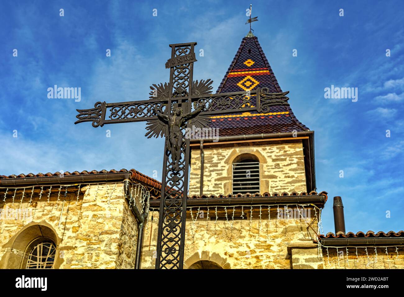Kruzifix und Glockenturm mit polychrom verglastem Majolikaturm der Kirche, die San Martino gewidmet ist. Villefontaine, Departement Isère, Frankreich Stockfoto