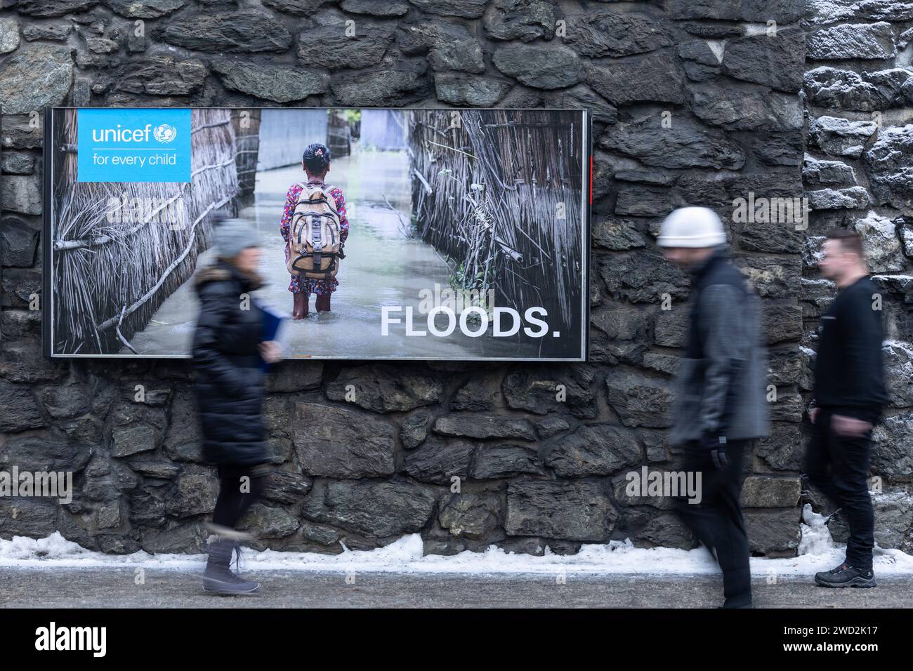 Davos, Schweiz. Januar 2024. Menschen gehen vor einem unicef-Poster mit der Aufschrift „Überschwemmungen“. Die Jahrestagung des Weltwirtschaftsforums gilt als einer der wichtigsten Treffpunkte für Spitzenpolitiker, Spitzenmanager und Wissenschaftler. Bei Debatten und vertraulichen Besprechungen geht es um Lösungen für globale Herausforderungen. Quelle: Hannes P. Albert/dpa/Alamy Live News Stockfoto