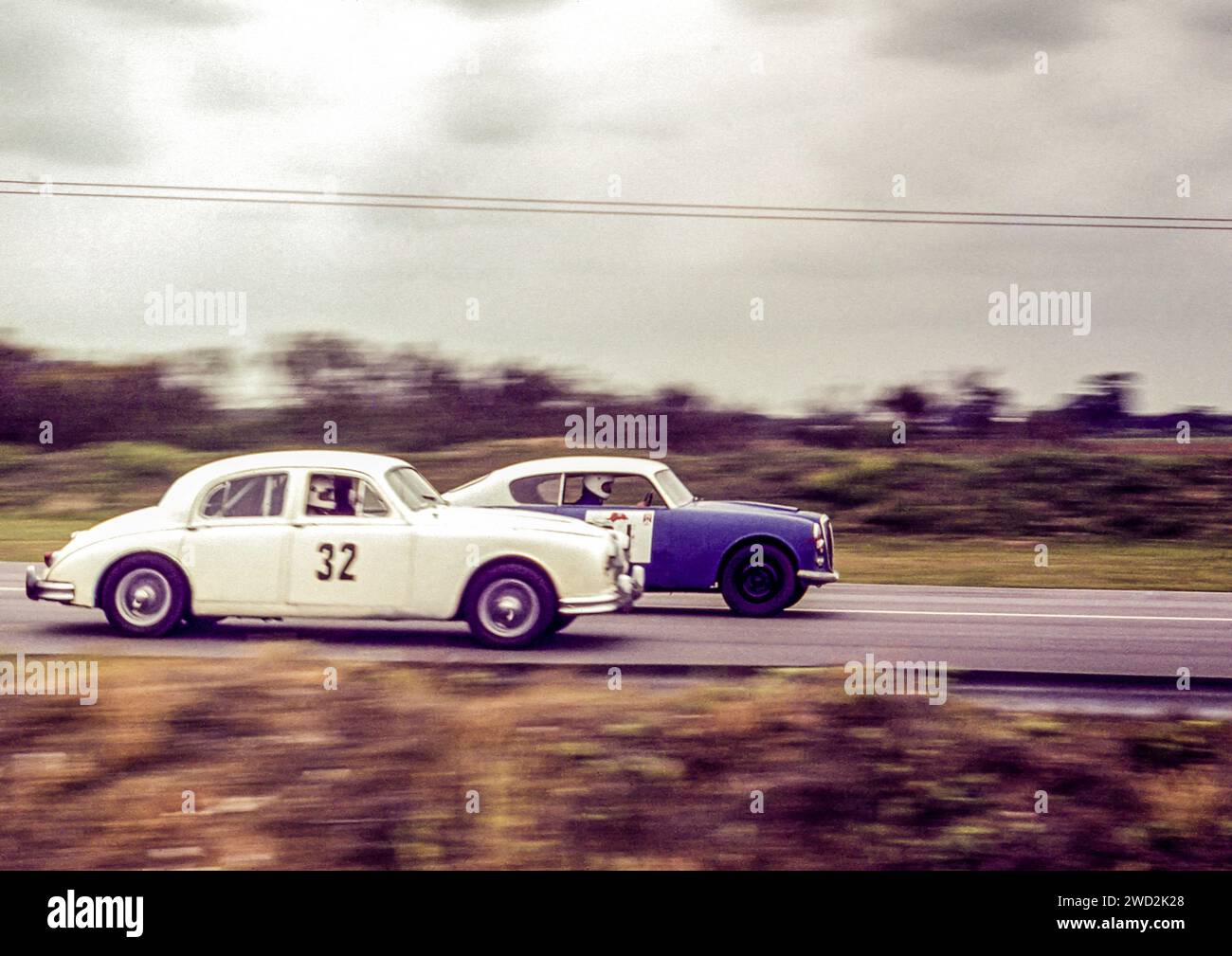 Ein weißer Jaguar MKII fuhr in den frühen 1970er Jahren gegen ein Blue Lancia Aurelia B20 Coupé auf dem Snetterton Circuit, Race Track, Norfolk. Ursprüngliches Archivbild. Stockfoto