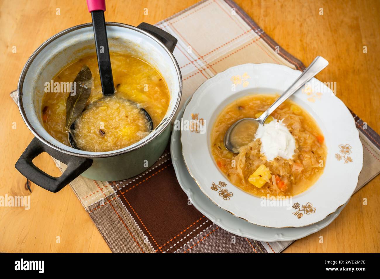 Kohlsuppe mit Kartoffeln im Zierteller und im Topf mit Schöpflöffel, Tischdecke auf Tisch, Nahaufnahme. Stockfoto