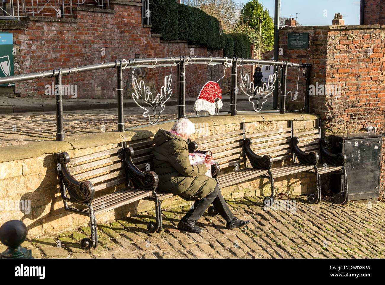 Ältere Dame, die auf der Sitzbank des Bürgermeisters sitzt, auf halbem Weg den steilen Hügel hinauf, Lincoln City, Lincolnshire, England, Großbritannien Stockfoto