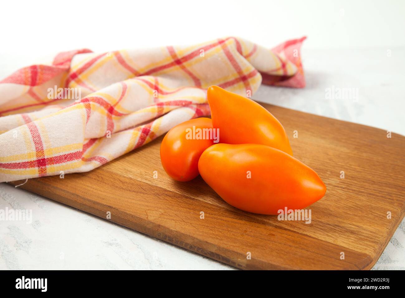 Hölzernes Schneidebrett mit mehreren ganzen Reifen saftigen gelben Tomaten und rotem Küchentuch auf weißem hölzernem Hintergrund. Gemüsesammlung. Stockfoto