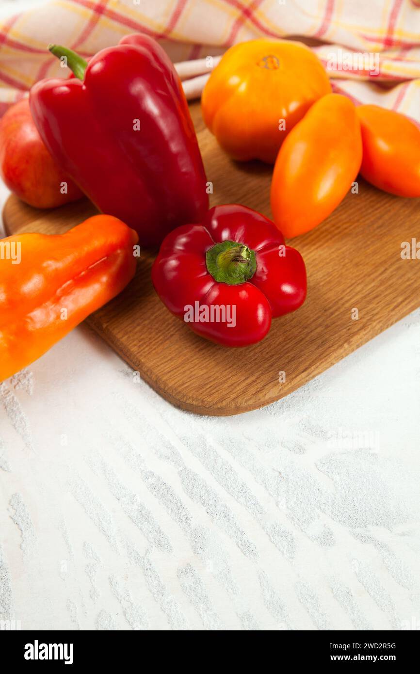Gemüsehintergrund. Schneidebrett mit verschiedenen ganzen Reifen, saftigen Tomaten und Paprika auf weißem hölzernem Hintergrund mit roter Küche Stockfoto