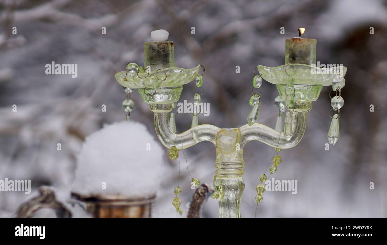 Ein Glaskerzenhalter. Eine silberne Kaffeekanne, die mit Schnee bedeckt ist. Stockfoto