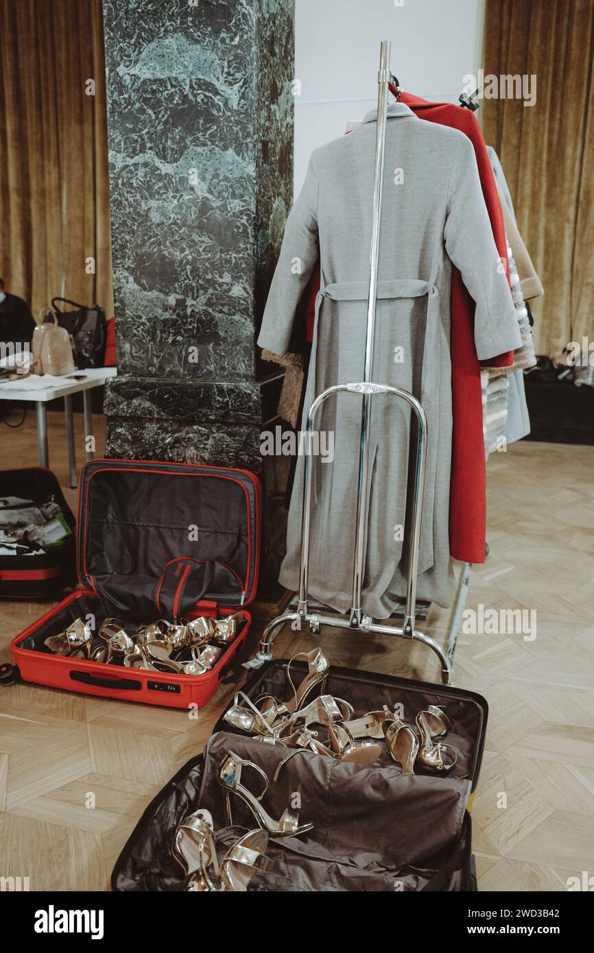 Modische Outfits hängen in einer Reihe und Koffer mit Schuhen im Backstage. Vertikale Modeschöpfung Stockfoto