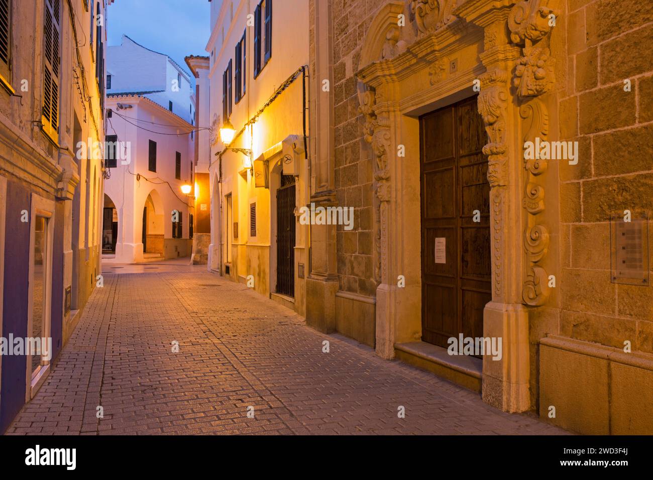 Ciutadella, Menorca, Balearen, Spanien. Blick auf die beleuchtete Altstadtstraße, Sonnenaufgang, die Kirchentür ist deutlich sichtbar. Stockfoto