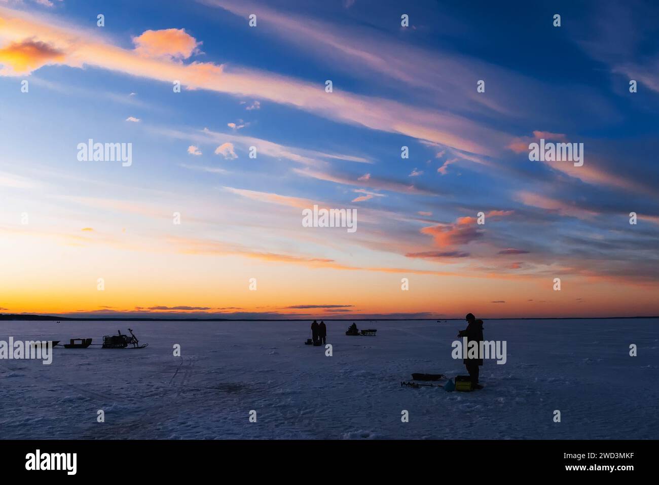 Silhouetten eines Fischers mit Angelrute an einem frostigen Winterabend bei Sonnenuntergang auf dem Fluss Stockfoto