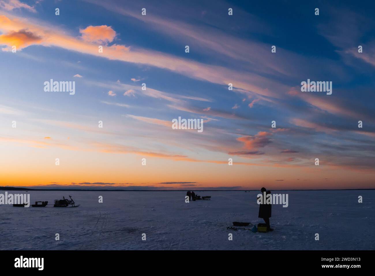 Silhouetten eines Fischers mit Angelrute an einem frostigen Winterabend bei Sonnenuntergang auf dem Fluss Stockfoto