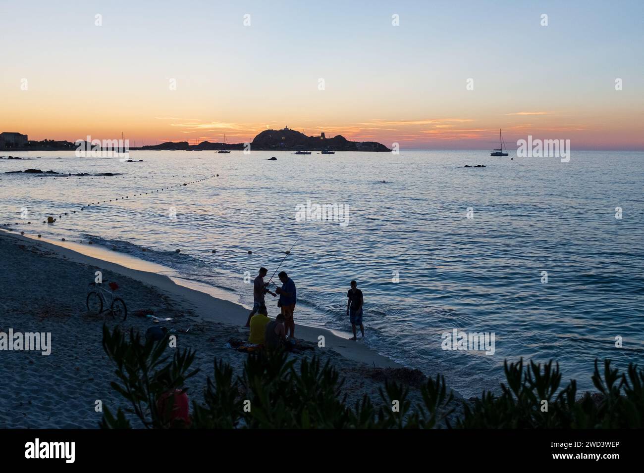 Ile Rousse, Korsika, 2017. Nach Sonnenuntergang fischen Menschen im Meer, mit der Ile de la Pietra und dem Leuchtturm im Hintergrund Stockfoto